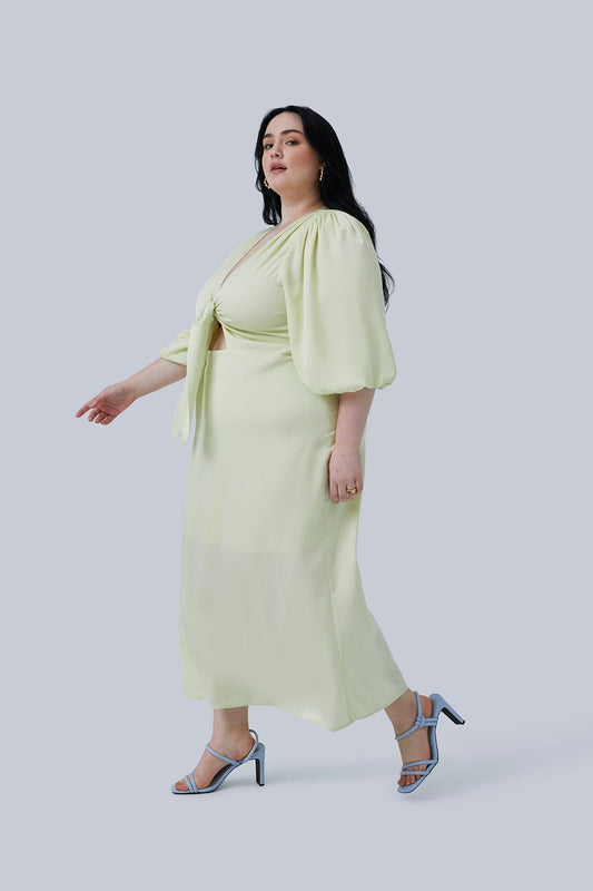 Side view of model walking wearing Allie Maxi Dress in Citron size 20. Bow ties in the front and hangs down in front of the front cutout. Dress by Gia IRL Plus Size Boutique & fashion for plus size women.