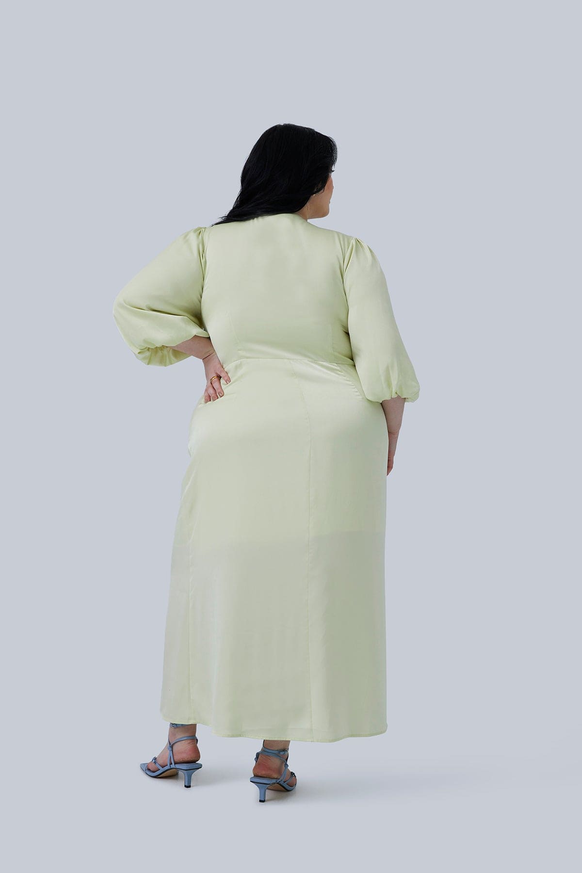 Back view of the Allie Maxi Dress for plus size women. Designed by Gia IRL. Model has hand on hips, dress has bubble sleeves and fabric is silky smooth hugging your curves perfectly.