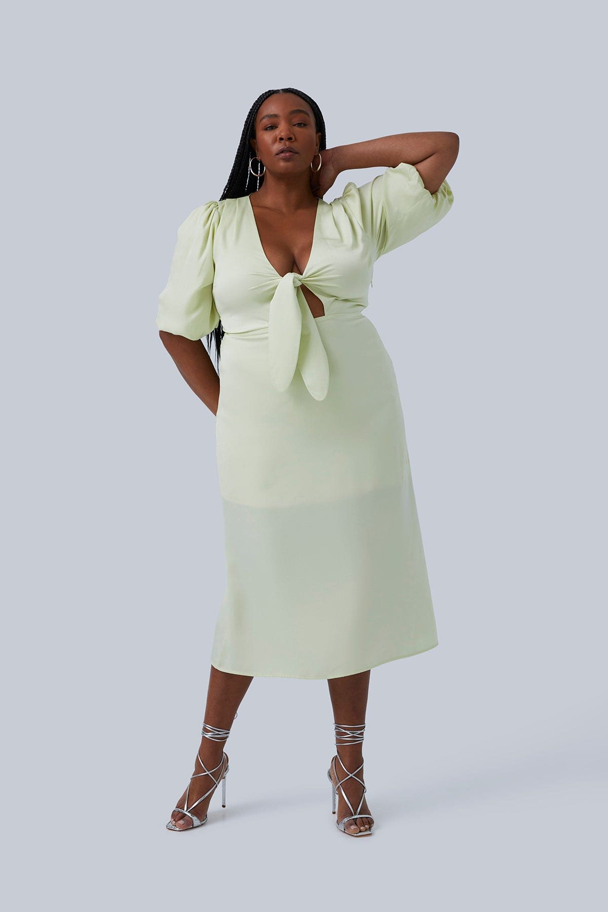 Front view of the Allie Maxi dress for plus size women size 14. Model has one arm on her neck and the other arm behind her back. Dress has tie in the front and can be worn without a bra.