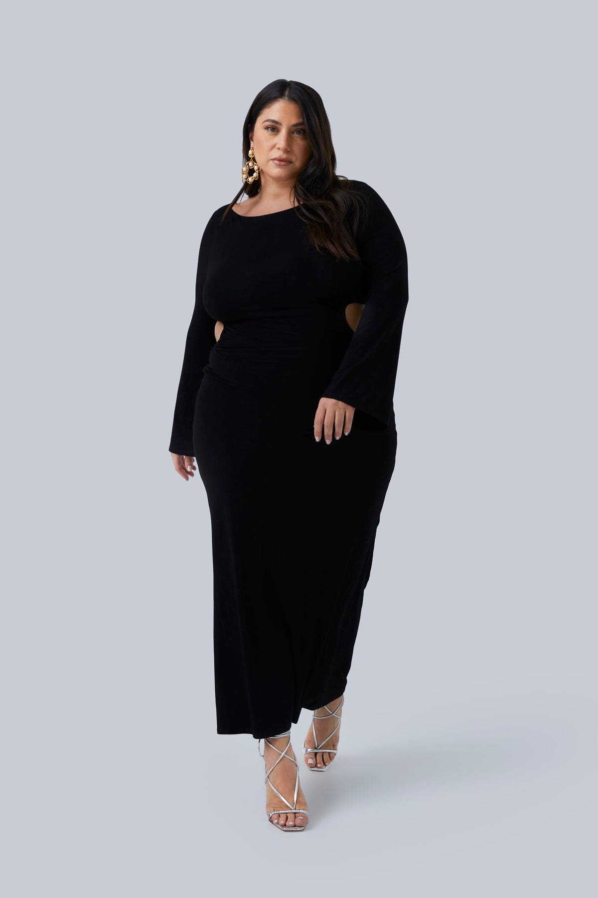 Full look of the Gabrielle Maxi plus size dress by Gia IRL. This dress has 2 layers of buttery fabric the hug your curves. Model is taking a step forward and her shoes are visible. Dress goes to ankles.