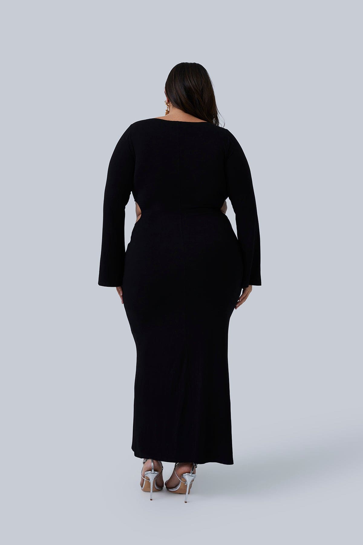 Back view of the Gabrielle Maxi dress. Long double-layered stretchy maxi dress for plus size women. Model is standing with hands by her side showing flared sleeves. Dress goes to ankles.