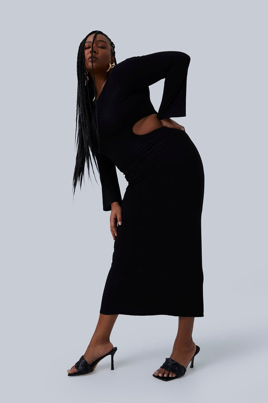 Plus size model doing a sassy side bend with hand on hip. Dress is Gia IRL the Gabrielle Maxi in black. Model is wearing this plus size long black dress with black mules.