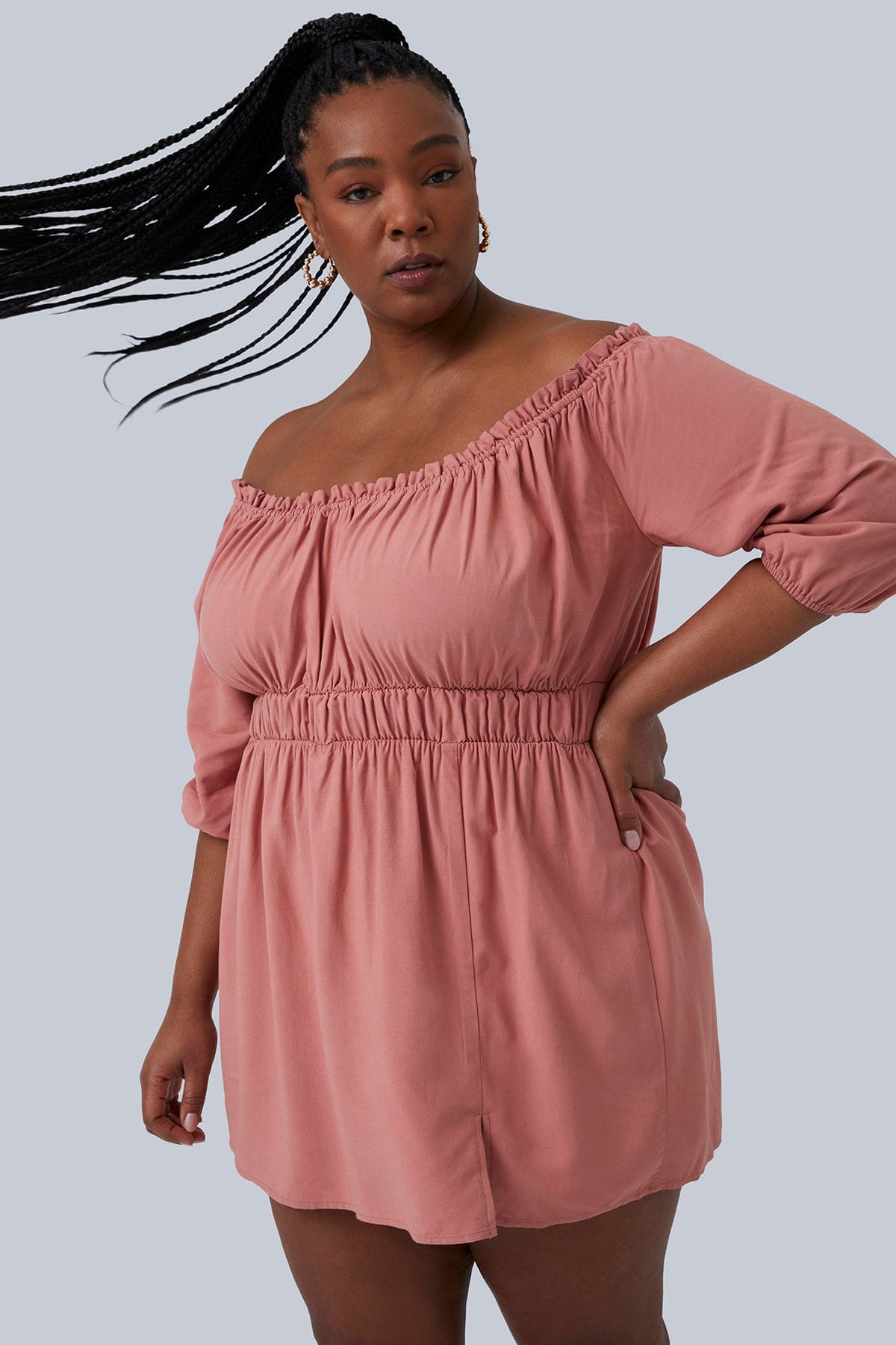 Model swinging her pony tail with braids while wearing the Gianna Mini Dress from Gia IRL Plus Size Boutique. Dress is in blush color and size 1X. Dress is slightly off the shoulder and a tiny peek-a-boo slit in the front.