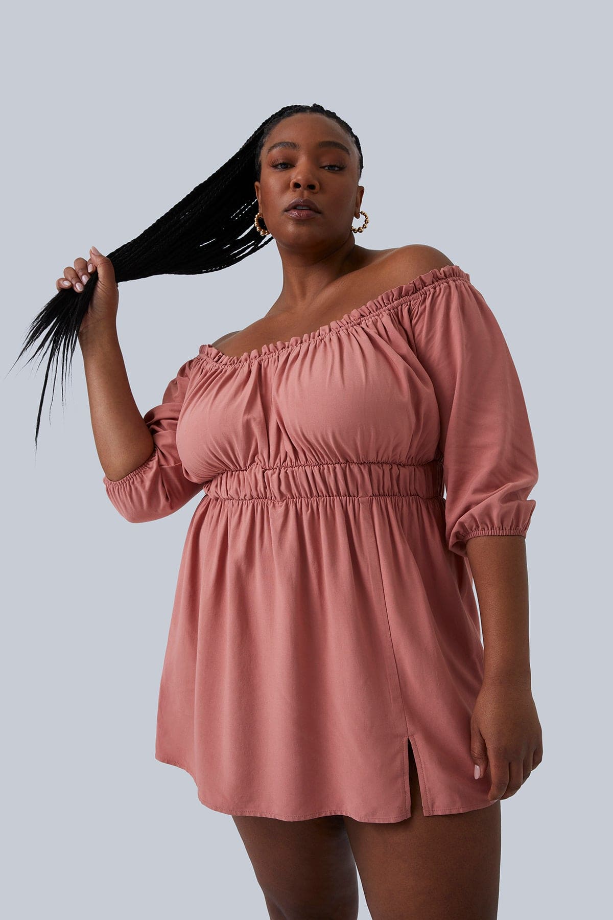 Plus size model wearing Gianna Mini Dress in blush size 1X. She is holding her long, braided pony tail in her hands and leaning back. Little, sexy slit in the front. Shop Gia IRL Plus Size Boutique.