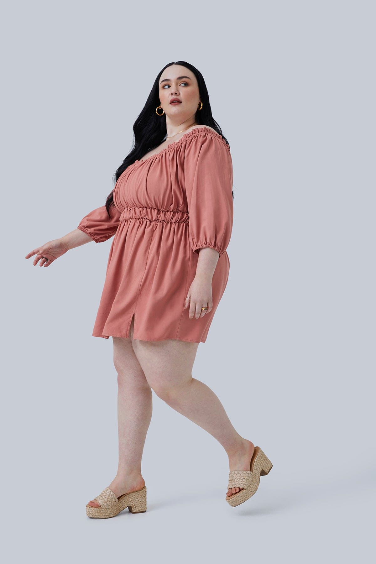 Side view of the Gianna Mini Dress in size 3X from Gia IRL Plus Size Boutique. Model is stepping to the side and looking up and over her shoulder. Basic dainty jewelry with this dress for plus size women.