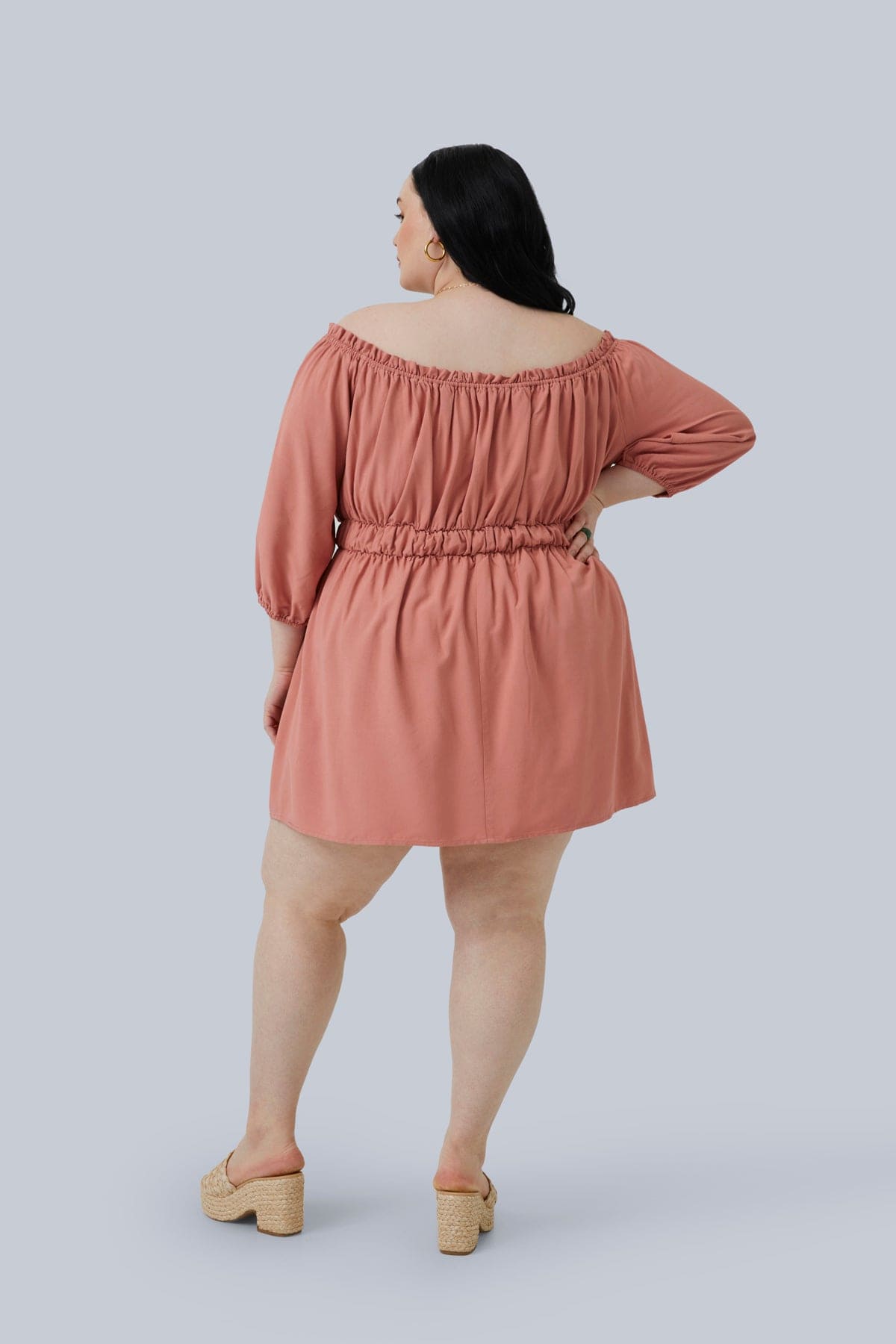 Back view of the Gianna Mini Dress in blush size 3X. Plus size model has one hand on hip and the dress is a little bit shorter than mid-thigh. Sexy, sassy and super cute plus size fashion for women. Shop Gia IRL Plus Size Boutique.