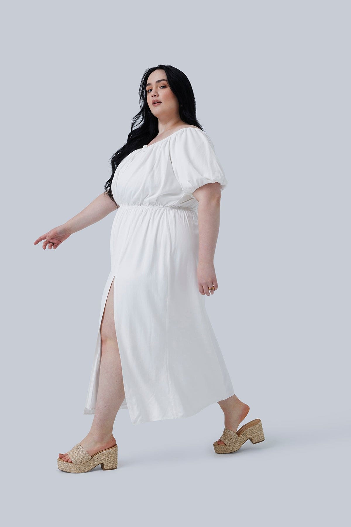 Side view of this plus size dress for women who LOVE fashion. Model is in the Gia IRL Gia Midi Dress size 3X in white. Model is taking a step and her long dark hair is over her shoulder.