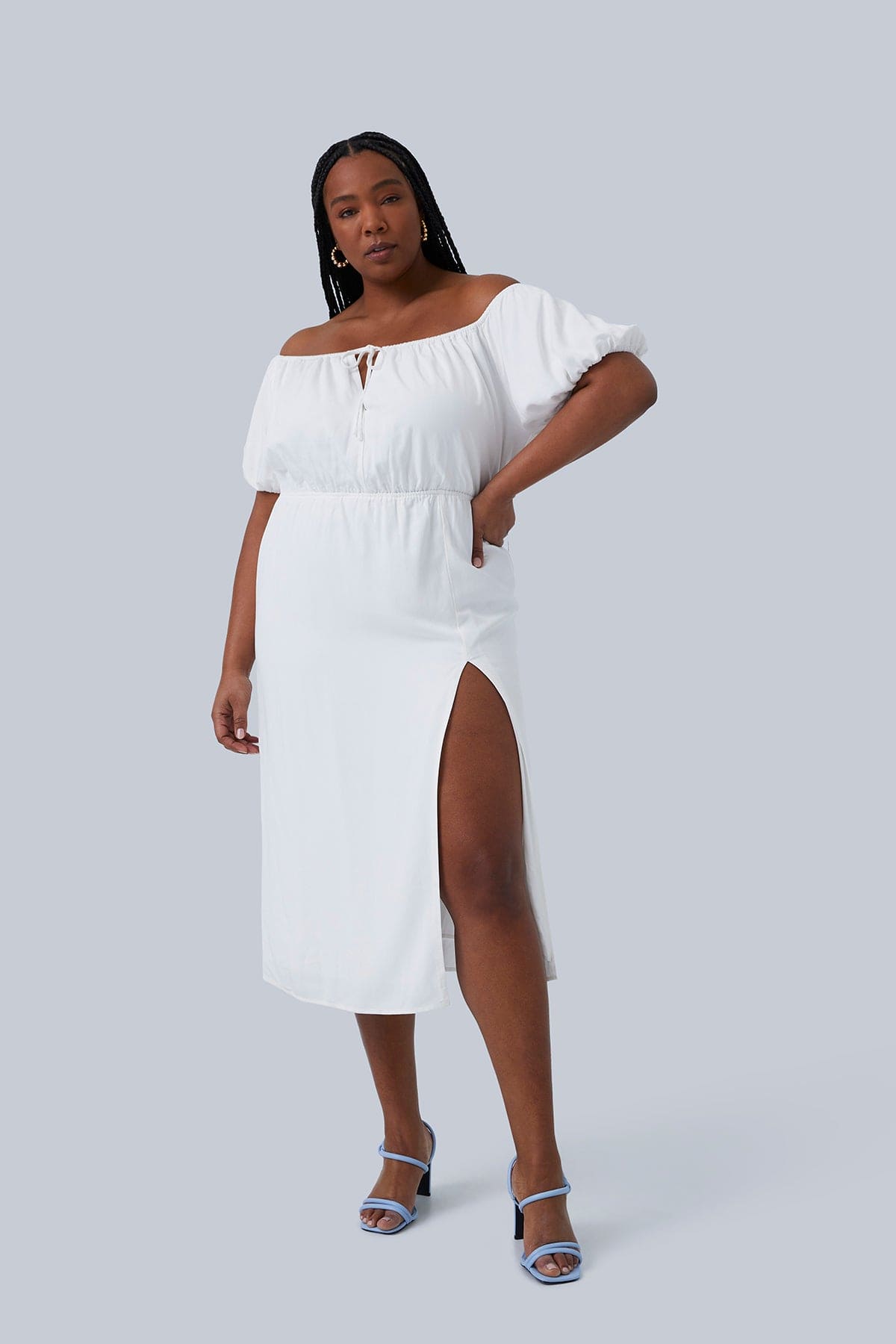 Gia midi dress size 1X is inspired by romantic Italian adventures. Off the Shoulder Midi Dress with Puff Sleeve, Center Front Keyhole with Ties, Thigh High Slit. Plus size model has hand on her hip and leg stepping forward to highlight the slit.