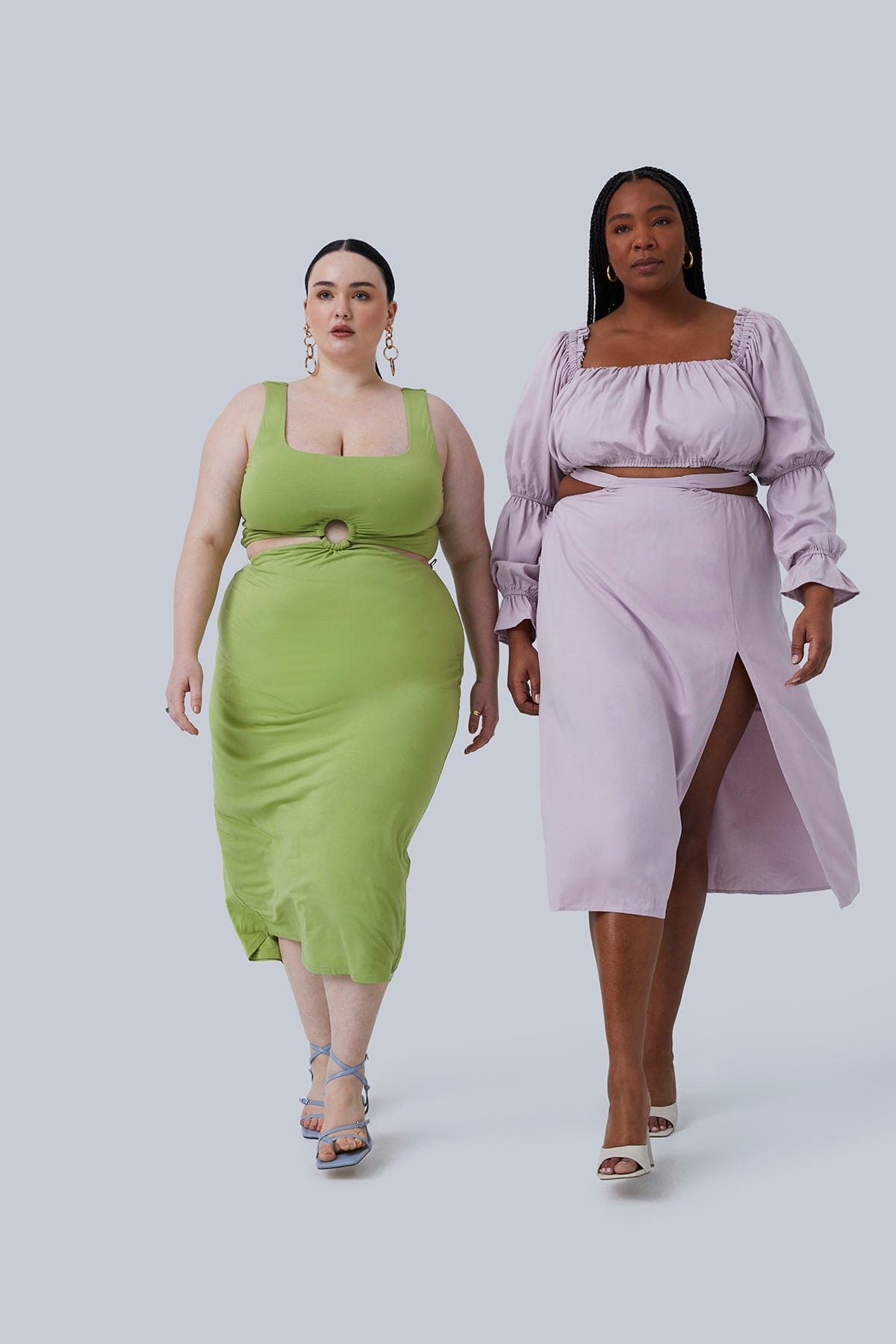 Two Plus Size Models walking towards the camera. Model on the left is wearing Gigi Midi in Pistachio size 2X, model on the right is wearing the Gia Top and Gia Skirt in Lilac size 2X. All designed by Gia IRL Plus Size Boutique.