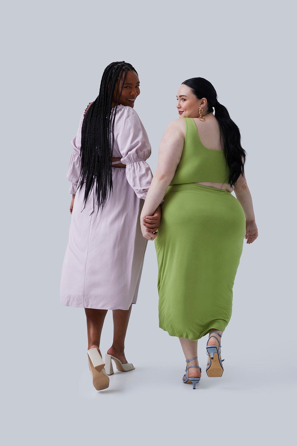 Two plus size models wearing Gia IRL Plus Size Boutique walking and holding hands and looking over their shoulders. Model on left in Gia Top & Gia skirt size 2X, model on the right in Gigi Midi Dress size 2X for Plus Size Women.