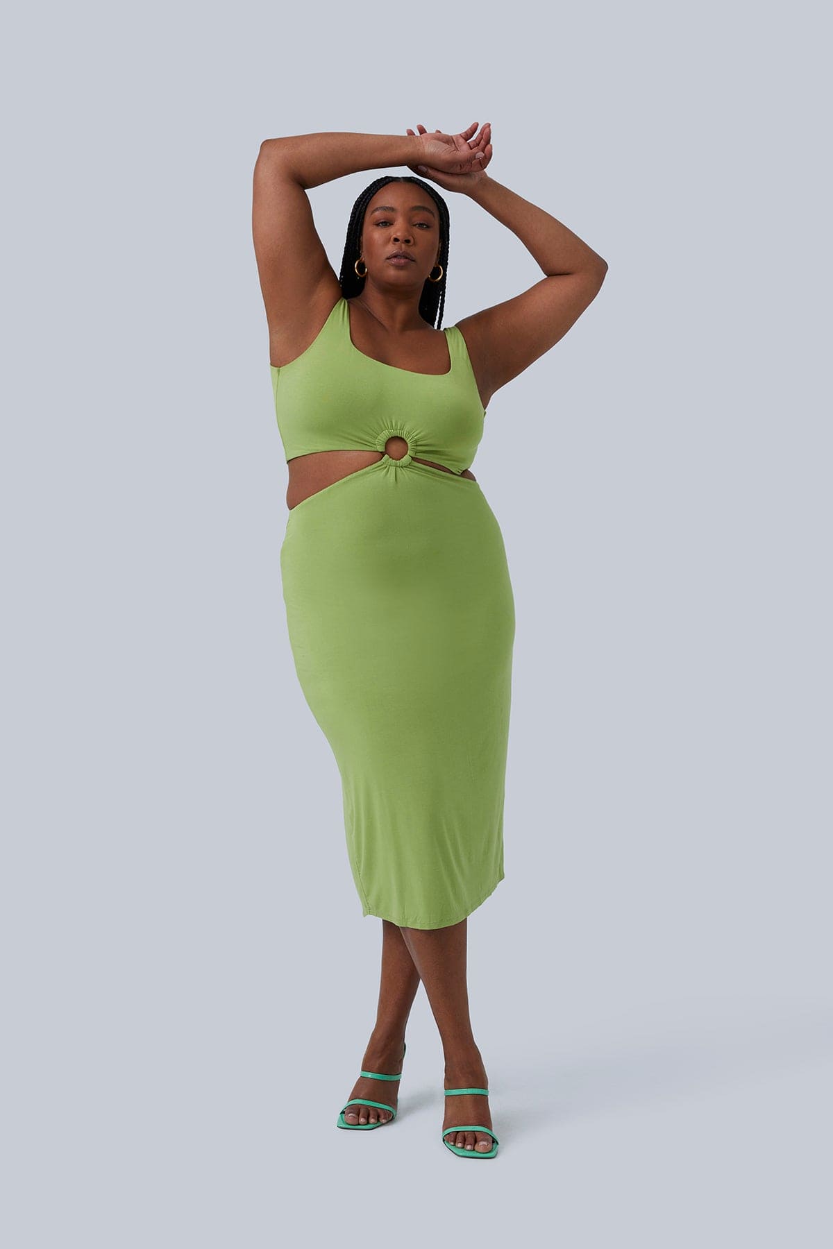 Full body front view of Gigi Midi dress on plus size boutique model in size 1X color pistachio. Fitted, stretchy fabric length to mid thigh. Model is standing, has arms over head and legs crossed.