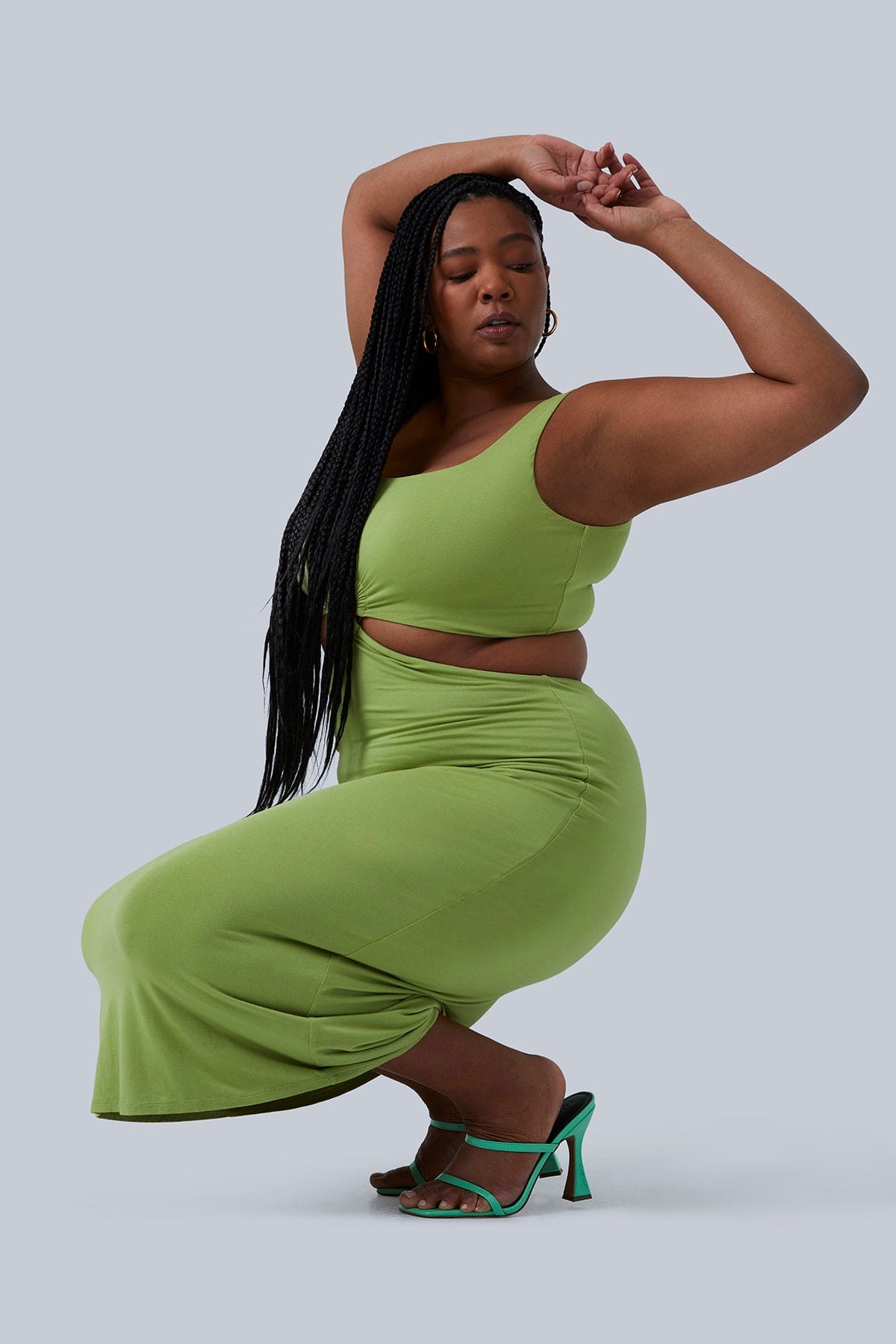 Plus size model squatting down and looking over her shoulder in Gigi Midi Dress by Gia IRL Plus Size Boutique. Dress is paired with turquoise heels and in size 1X.