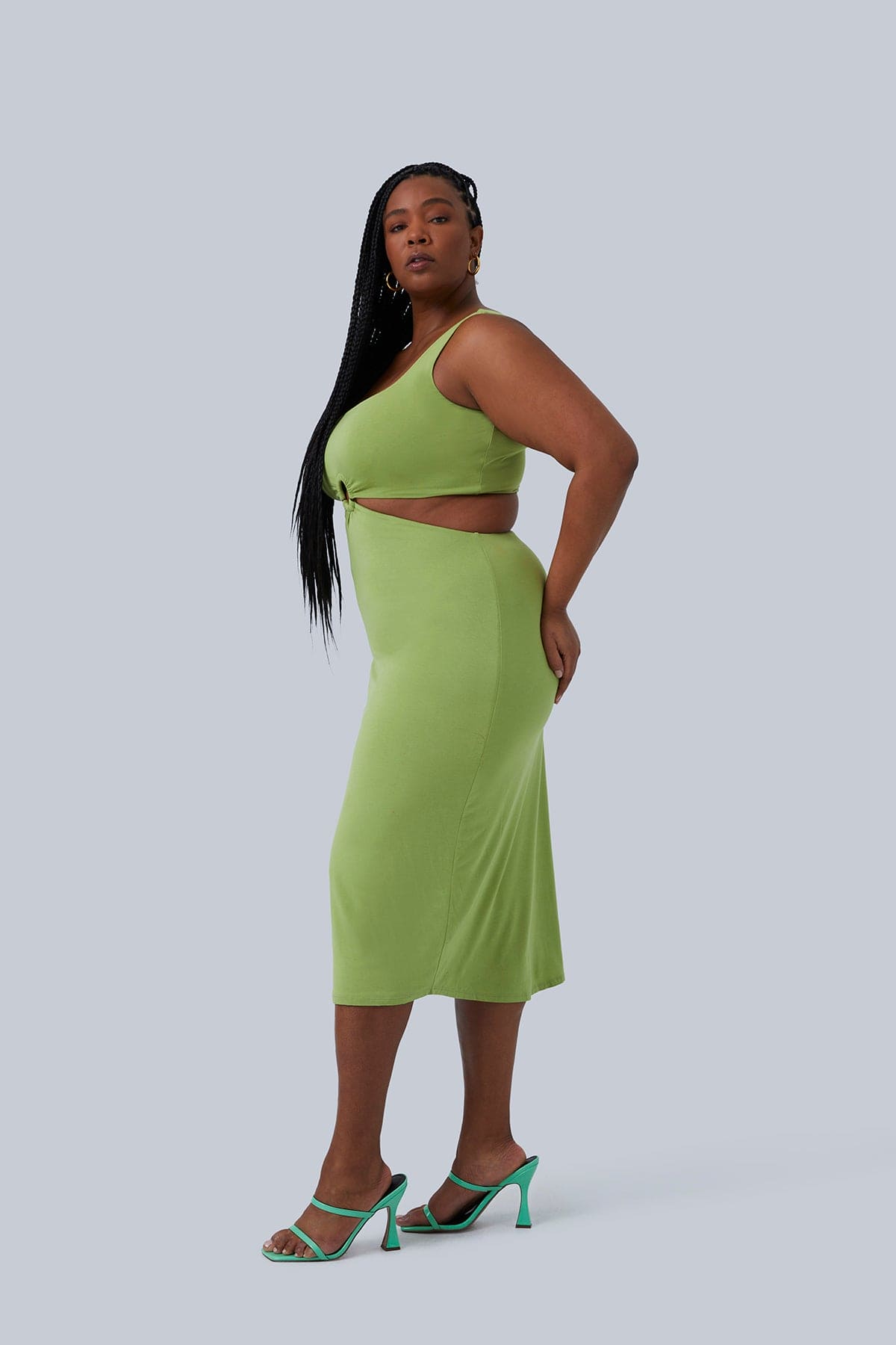 Side view of the Gigi Midi Plus Size Dress size 1X in Pistachio by Gia IRL. Model has hands on her low back and long black braids over shoulder. Dress goes to mid calf.