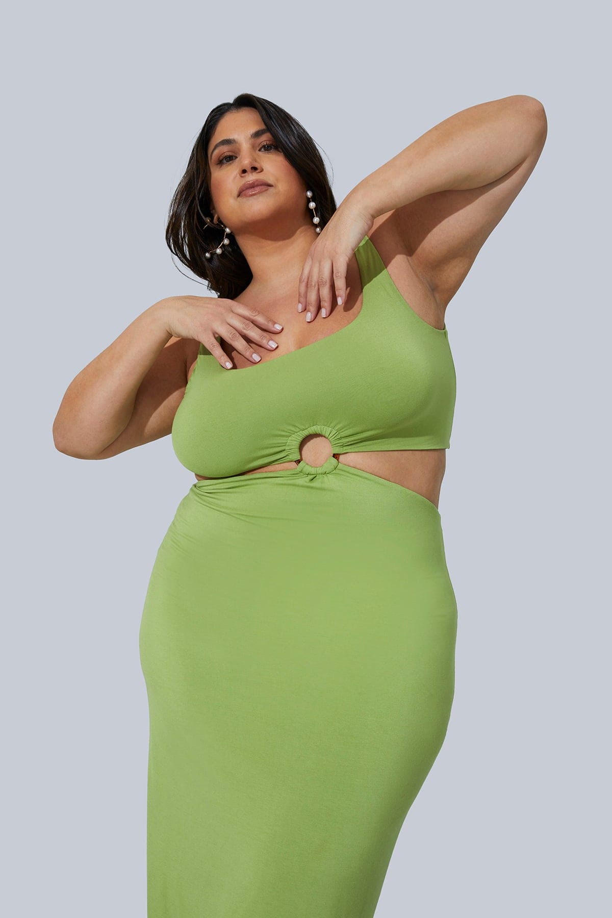 The Gigi Midi Dress from Gia IRL in Pistachio up close and personal. Model is standing with hands near chest and is leaning to the right highlighting the side cutout detail. Model wearing size 1X.