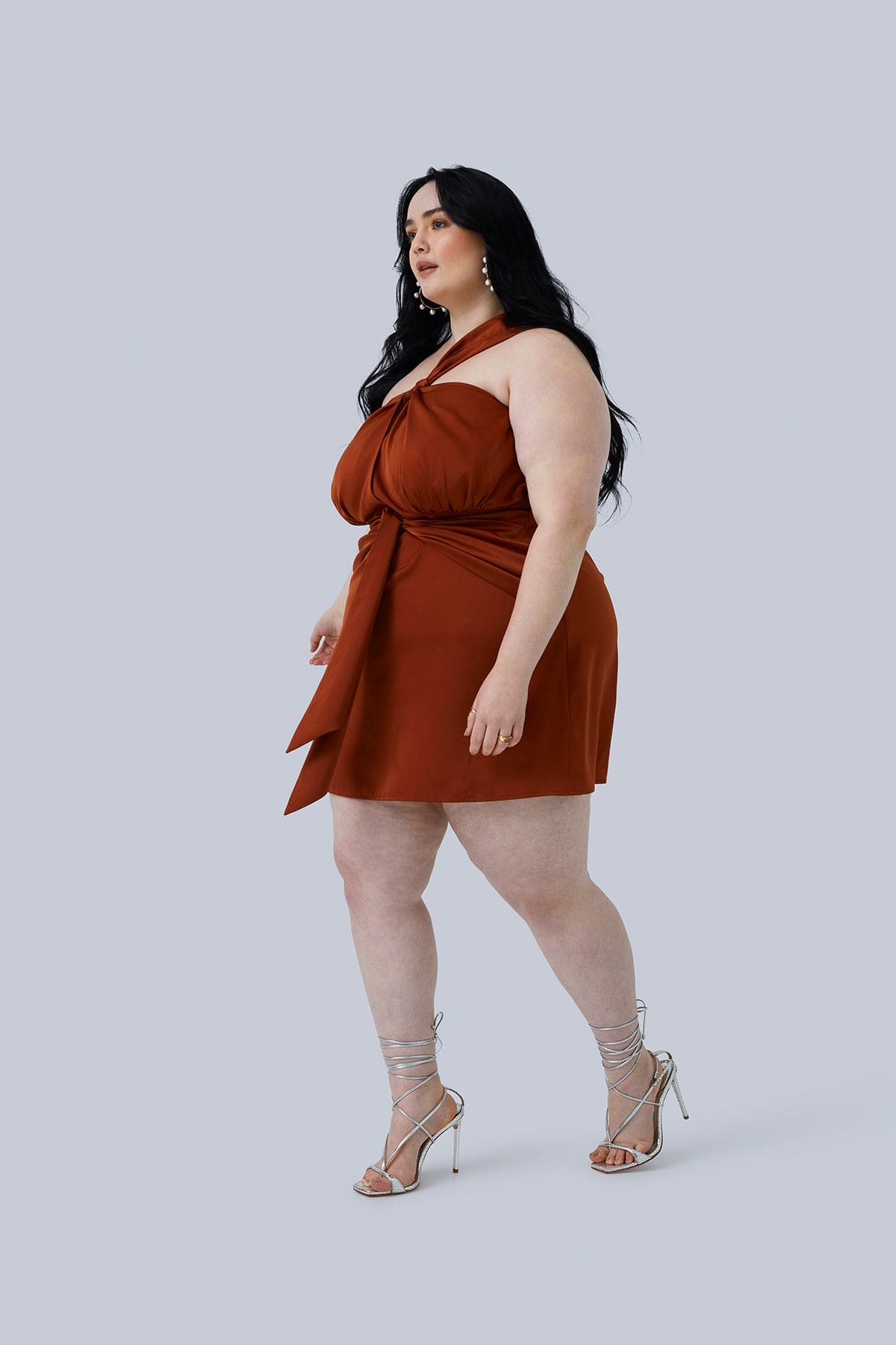 Full body shot of the Maya Mini Dress from Gia IRL Plus Size Boutique. Dress is silk and rust color, worn with strappy heals by plus size model with long dark hair size 18.