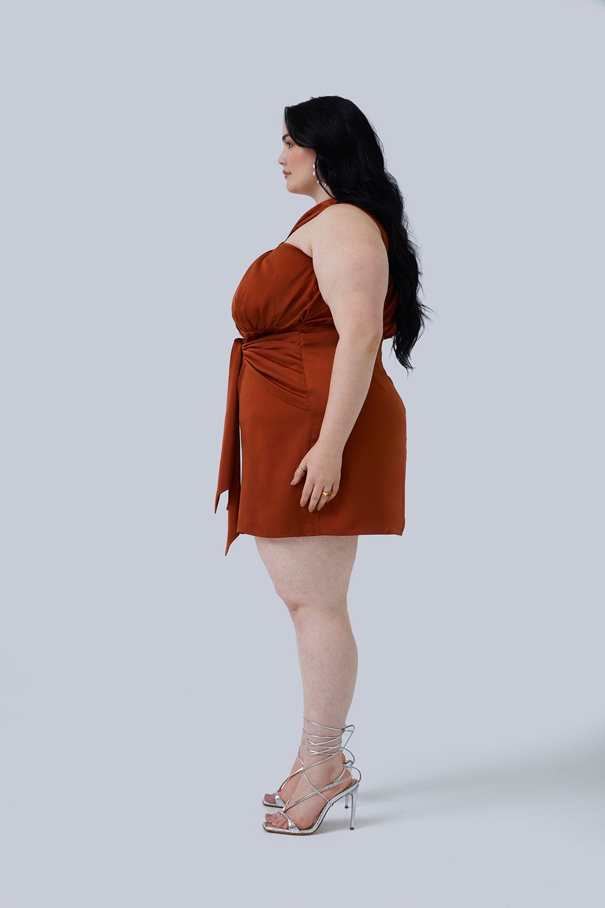 Side view of the Maya Mini Dress in Rust size 18. The silky fabric lays perfectly and dress hits about mid thigh for curvy women. Perfect dress for plus size women into fashion.